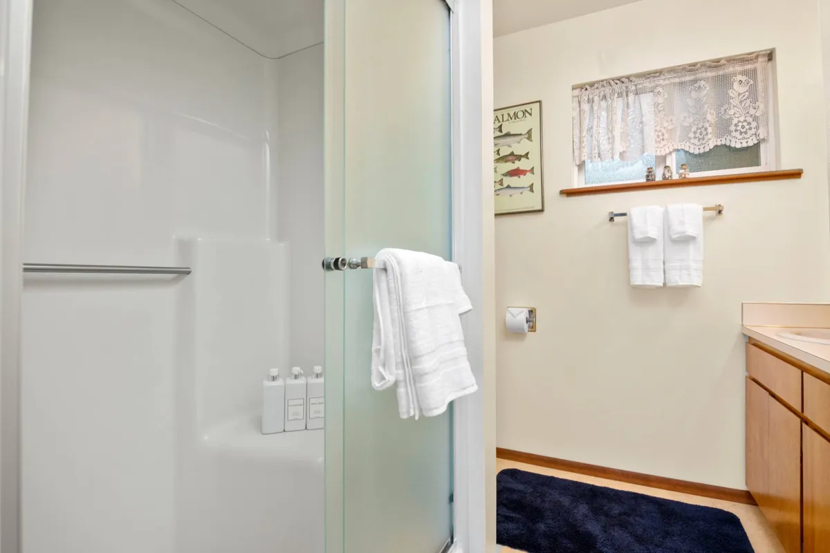 A serene bathroom with a glass shower enclosure, white towels, wooden vanity, and framed fish art, creating a calm and inviting space for personal care.