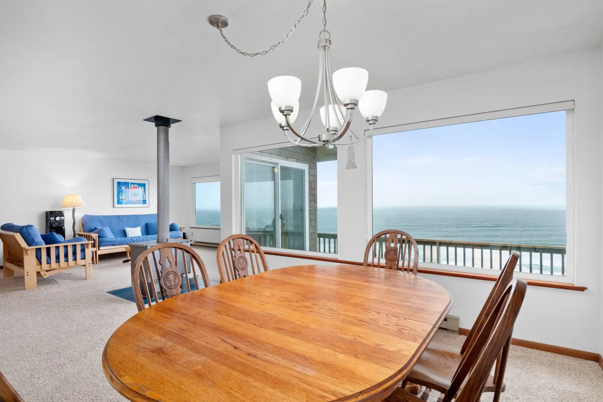 The photo presents a large dining table positioned near expansive windows, granting unobstructed views of the ocean. A stylish chandelier hangs above, and the table is set for a cozy gathering. The mood is warm and welcoming, perfect for celebratory meals or casual family dinners.