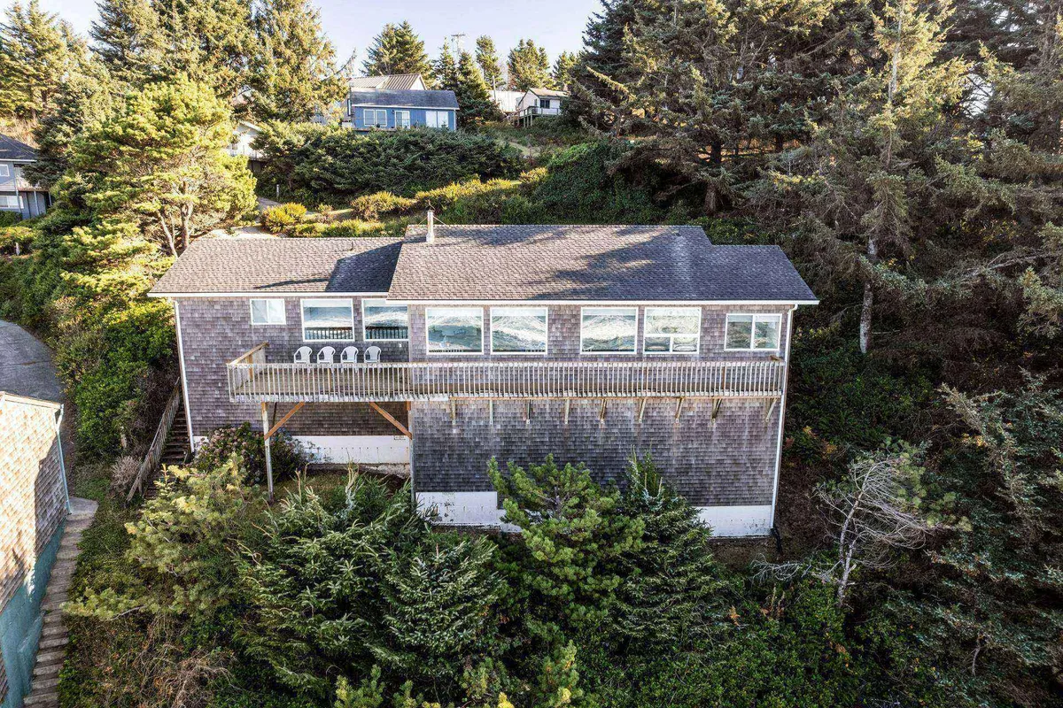 A wide exterior view of the house, its spacious deck, and the lush trees surrounding the property. The deck is furnished and appears welcoming, perfect for relaxing or taking work breaks outdoors. The setting is tranquil, with plenty of greenery and a clear connection to nature.
