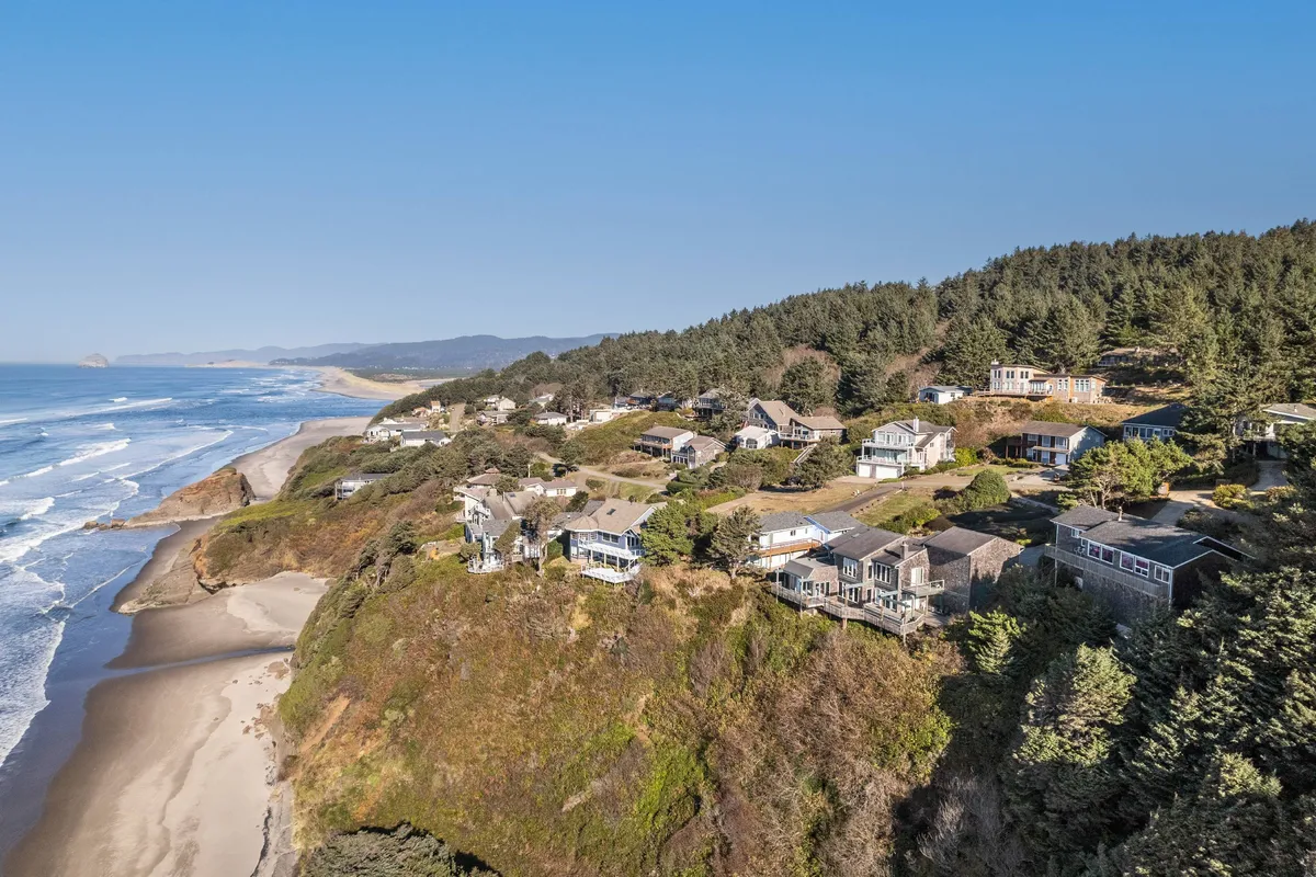 A sweeping view of cliffside homes overlooking an expansive ocean, sandy beach, and lush greenery below. The scene feels tranquil and invites outdoor exploration, making it ideal for activities like beachcombing, hiking, or simply soaking in the scenery.
