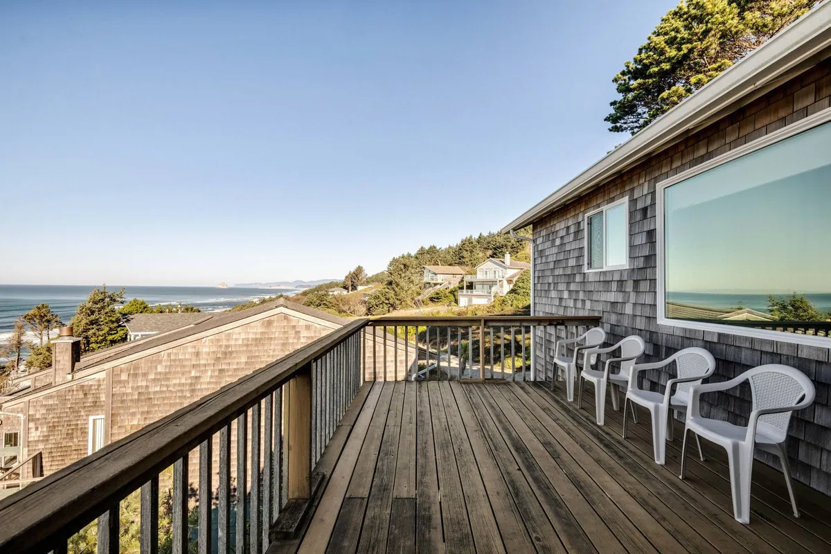 A tranquil wooden deck overlooking the ocean, surrounded by neighboring houses. The space is arranged for socializing, sunset watching, and stargazing, making it suitable for both intimate gatherings and lively barbecues.