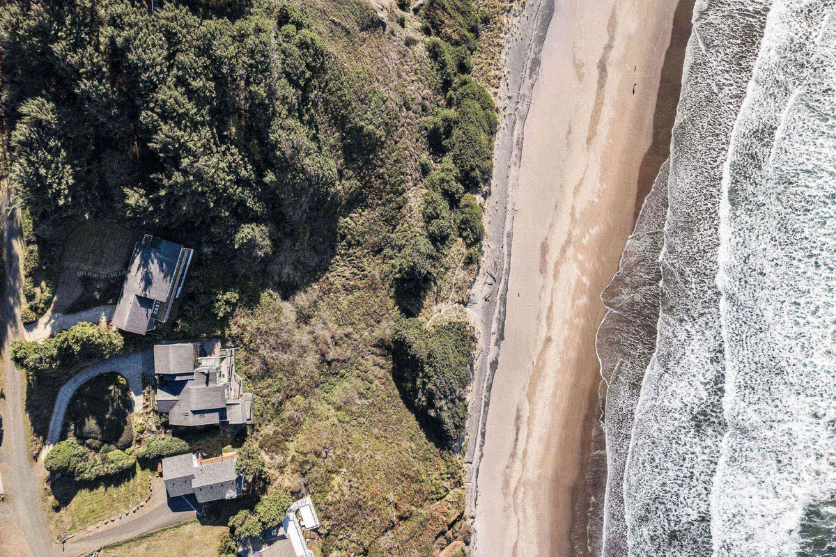 A panoramic ocean view with a sandy beach in the foreground, a few homes visible along the shoreline, and lush greenery providing a natural, calming backdrop. The scene is lively yet serene, perfect for families to enjoy beach walks, picnics, and connecting with nature.