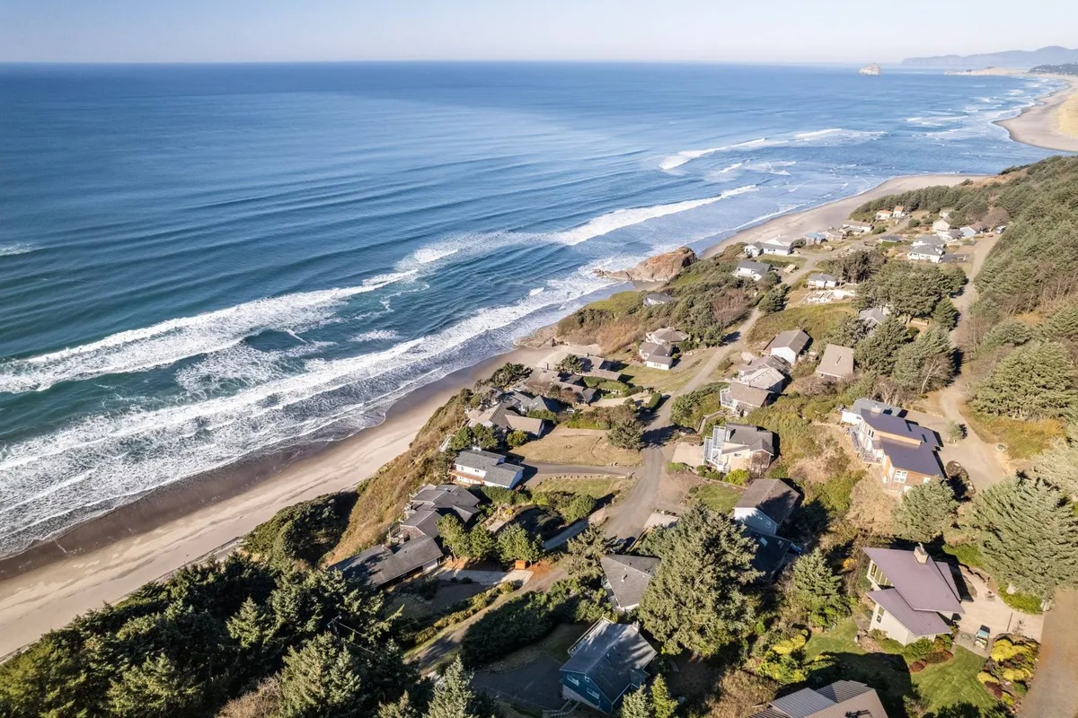 A tranquil coastal scene featuring a wide stretch of beach, rolling ocean waves, coastal homes nestled among trees, and a soft, inviting light. The image conveys opportunities for family beachcombing, sunset strolls, and outdoor play just steps from the home.
