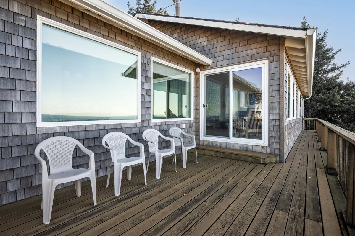 A cozy deck area with plastic chairs, large windows, and warm morning sunlight. The inviting mood is perfect for enjoying a quiet cup of coffee or relaxing with friends while gazing at the sunrise or stargazing at night.